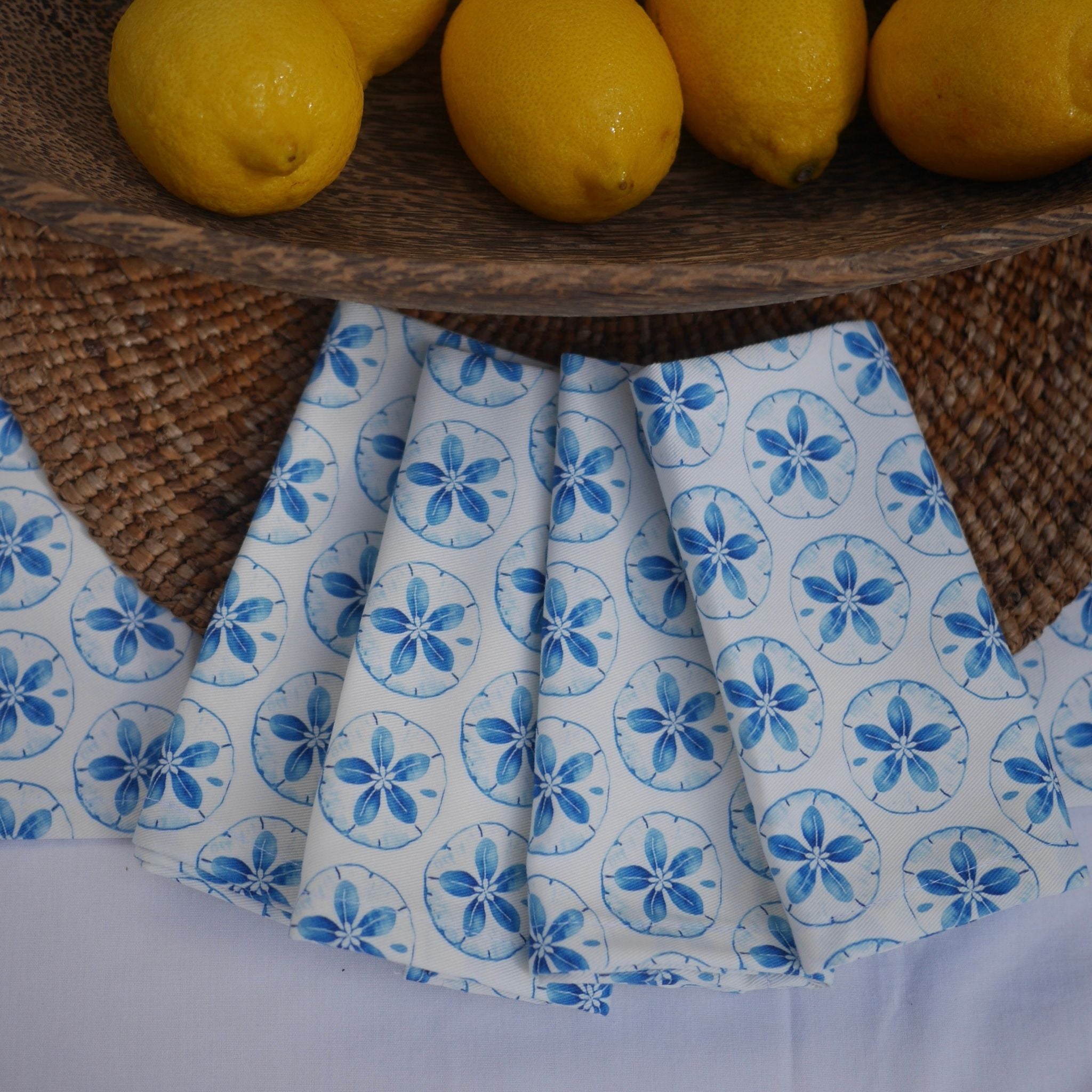 Folded fabric with blue floral pattern on a woven surface with lemons