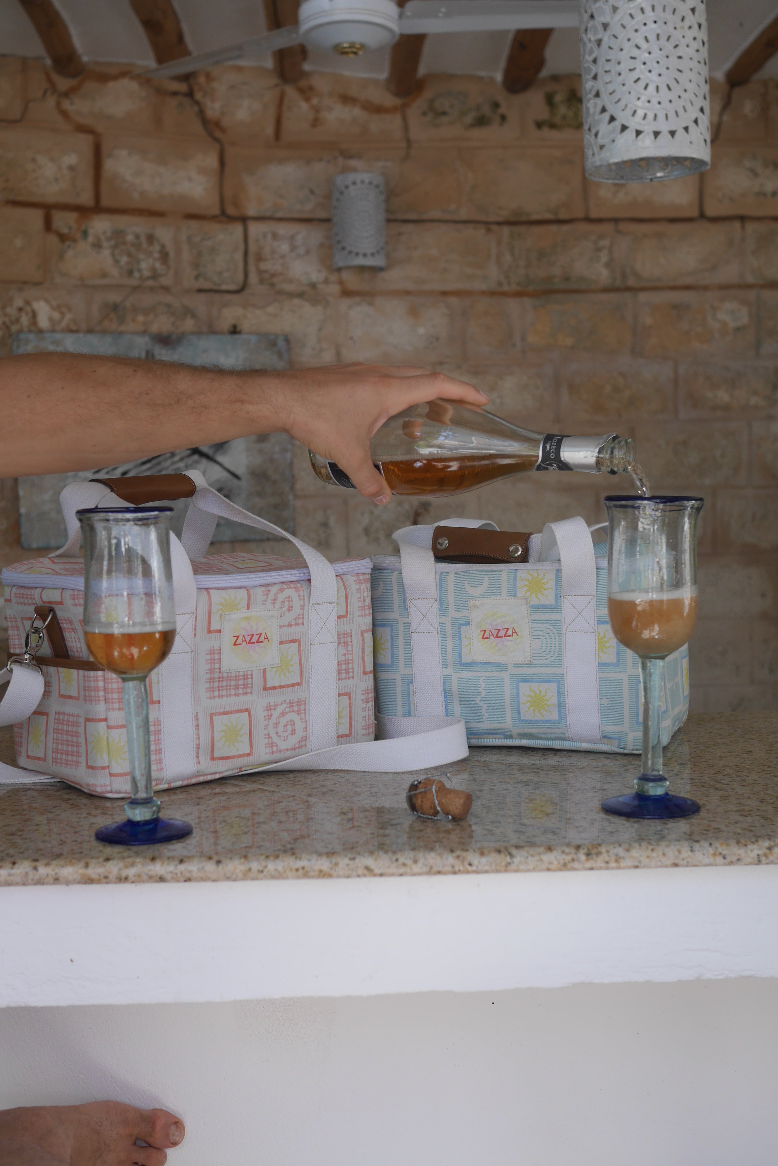 Person pouring a drink into a glass with ZAZZA cooler bags in the background.