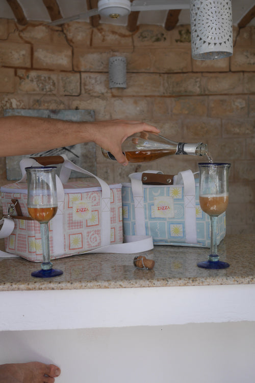 Person pouring a drink into a glass with ZAZZA cooler bags in the background.