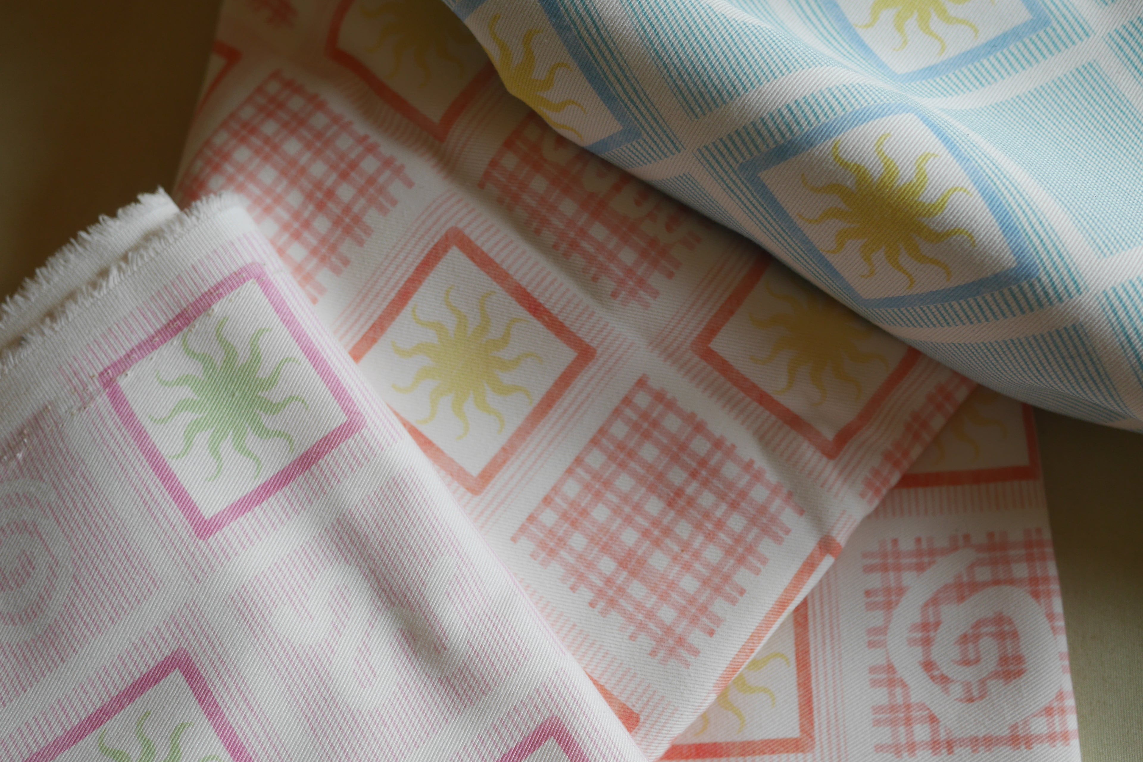 Close-up of ZAZZA  picnic collection patterned fabric with sun and circle designs on a neutral background