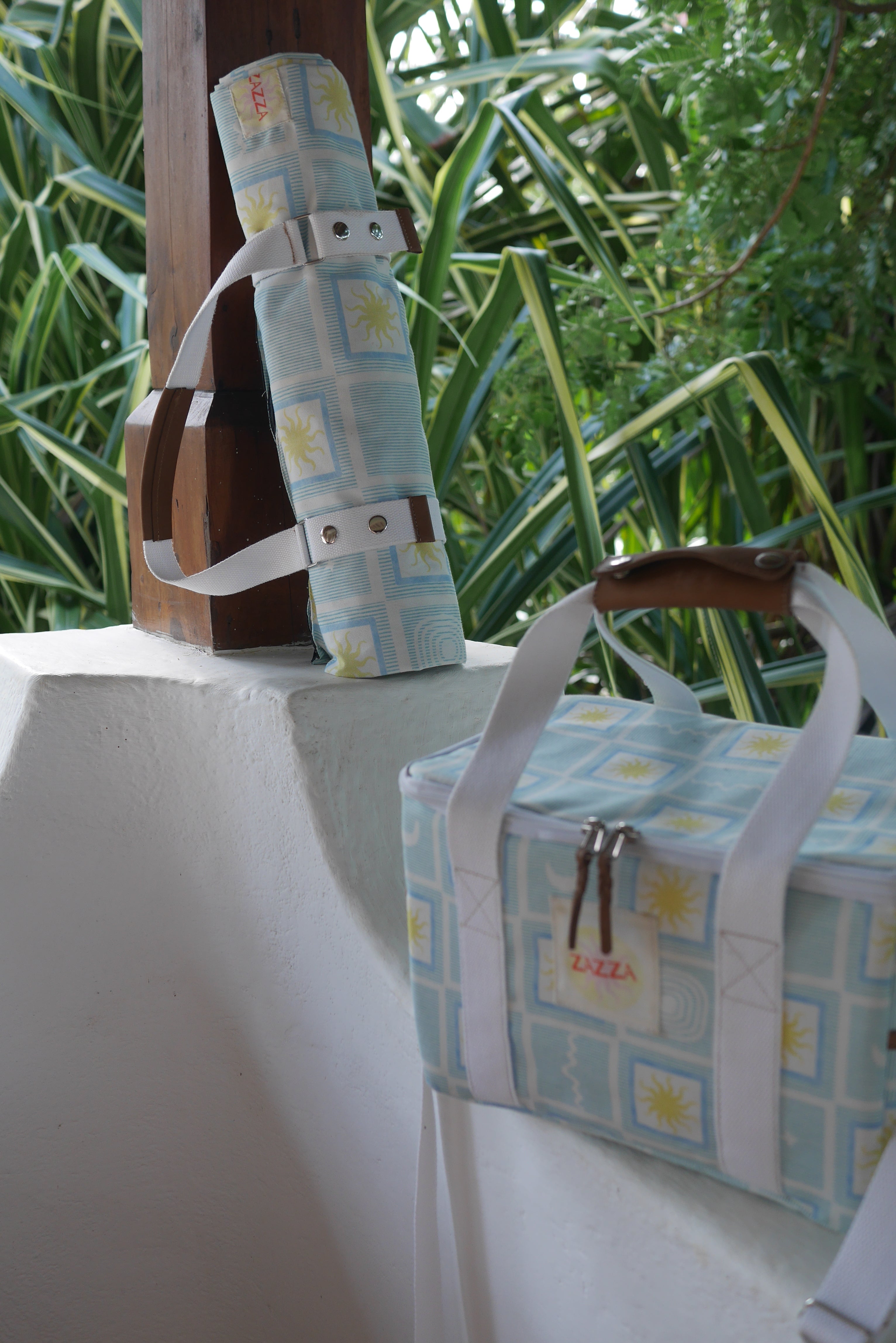 ZAZZA blue picnic blanket & cooler bag, styled on a white ledge and lush green background  