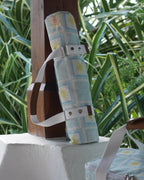 ZAZZA blue picnic blanket, rolled &  to a wooden surface, with greenery in the background