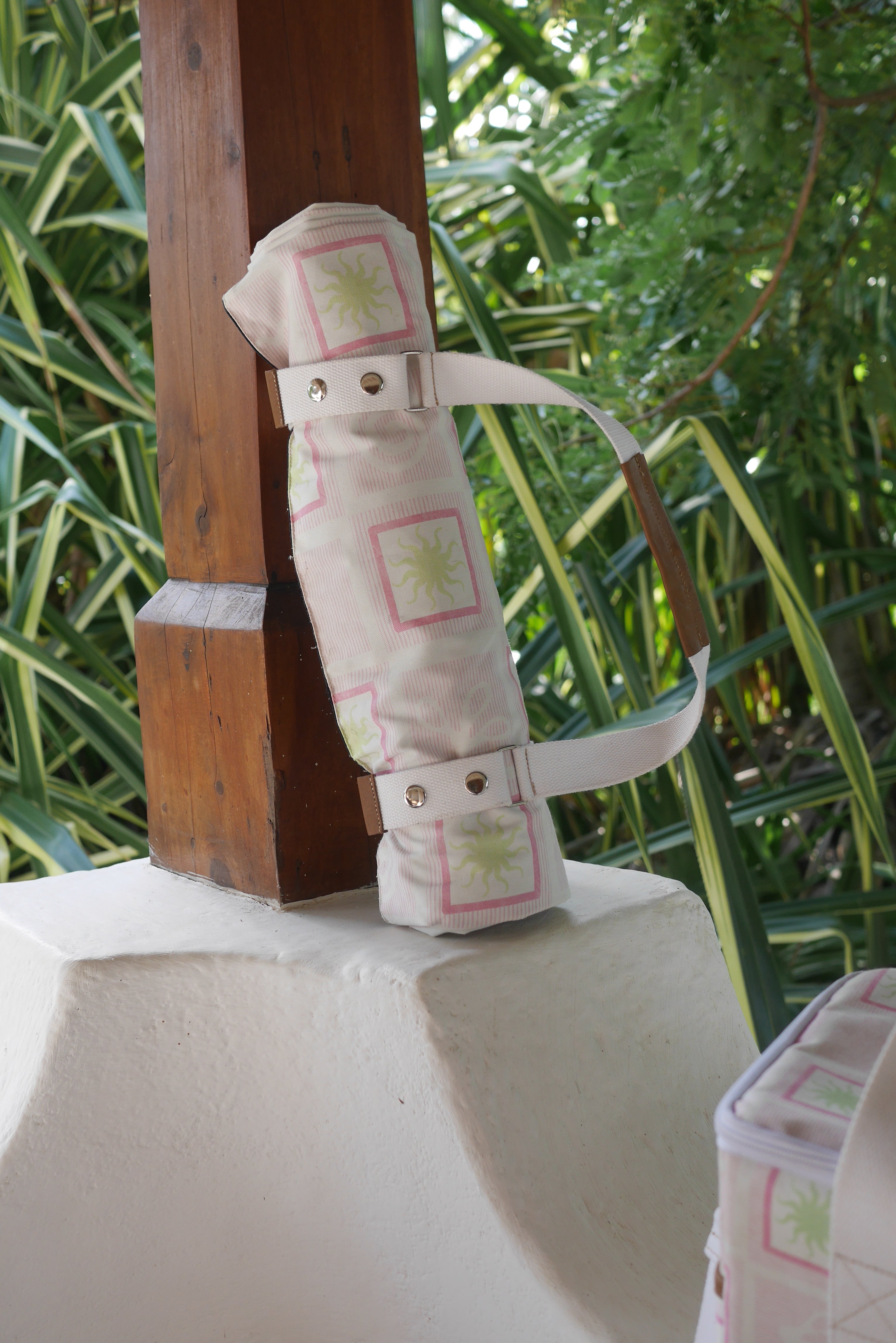 ZAZZA pink picnic blanket, rolled &  to a wooden surface, with greenery in the background