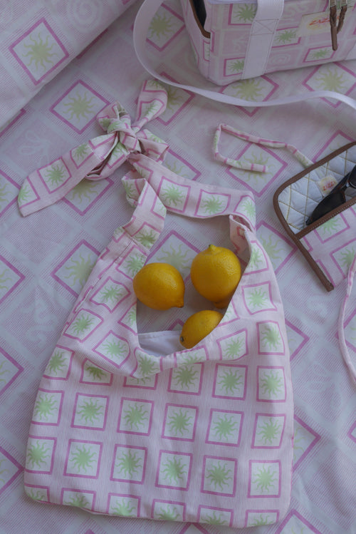 Flat lay image of ZAZZA Pink tote bag with lemons on a matching fabric background (picnic blanket) & other products from the picnic collection