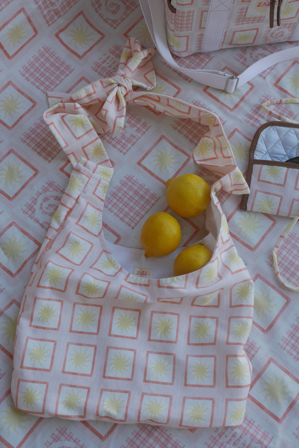 Flat lay image of ZAZZA Red  tote bag with lemons on a matching fabric background (picnic blanket) & other products from the picnic collection